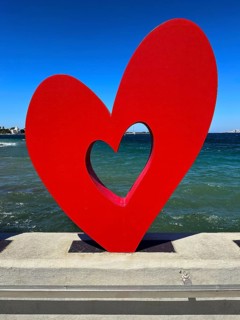Red heart sculpture in front of blue sea and sky, romantic modern art on concrete base, Kos Town,