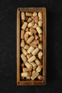 A wooden box is filled with an assortment of wine corks, showcasing various shapes and textures