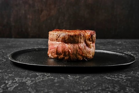 A perfectly cooked filet mignon rests on a sleek black plate, showcasing its rich color and