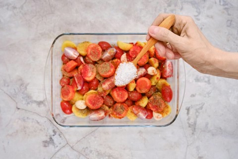 A hand sprinkles salt over colorful fresh vegetables and seasonings, preparing a vibrant mix to