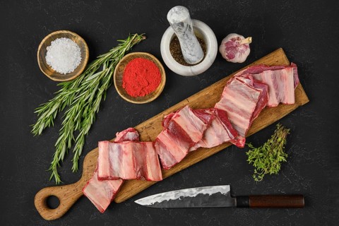 Fresh raw beef short ribs lay on a wooden cutting board alongside bowls of seasoning, herbs, and a