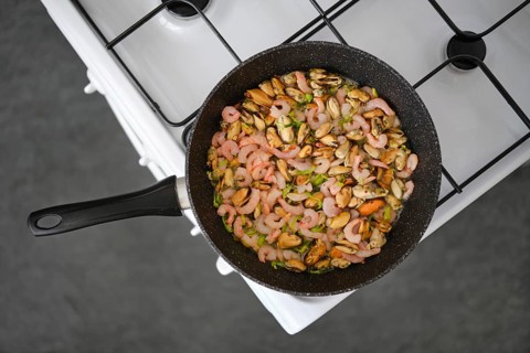 Seafood stir-fry with shrimp and mussels in a black pan, mixed with colourful herbs and spices on a