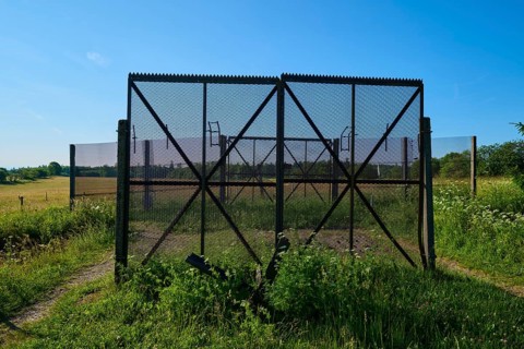 Border fence of the former inner-German border, surrounded by green meadows under a clear blue sky,