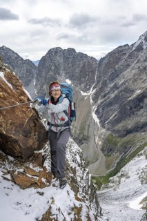 Mountaineer on a rope-secured path in a steep rocky mountain landscape with fresh snow in summer,