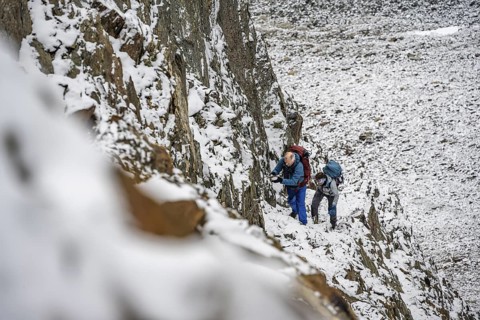 Mountaineer on a rope-secured path in a steep, rocky mountain landscape with fresh snow in summer,