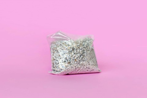 Small plastic bag containing ash of a pet cat after cremation on pink background