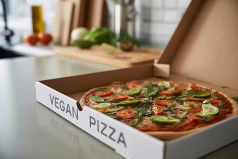 Freshly delivered vegetable pizza in box labeled vegan pizza on kitchen counter. Healthy