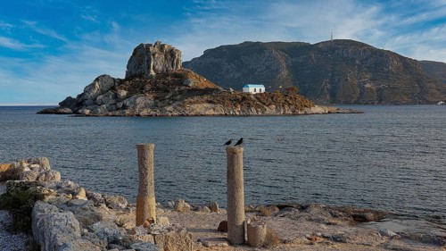 Stone columns in front of the sea with a view of an island under a slightly cloudy sky, Agios