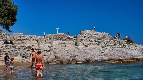 People and children exploring ancient ruins on the beach in sunny weather, Agios Stefanos Beach,
