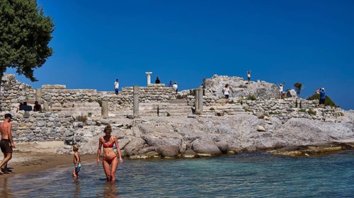 Families enjoy the day at ancient ruins by the sea with clear skies, Agios Stefanos Beach, Agios