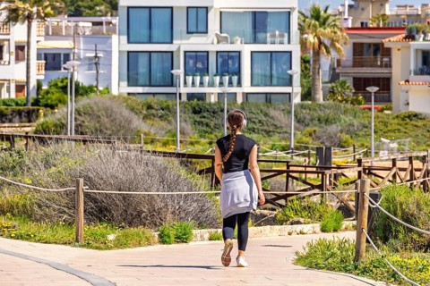 Young woman walking outdoors on a path in a residential area and listening to music with headphones