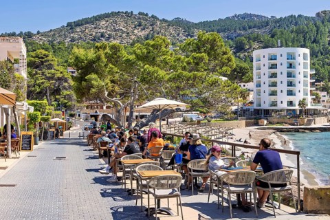 Tourists sitting in an outdoor restaurant on a boardwalk by the Mediterranean Sea at a tourist