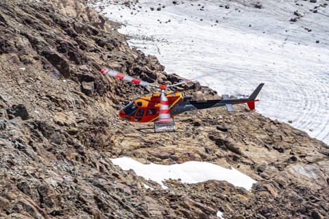 Red helicopter flies over glaciers in the mountains, Stubai Alps, South Tyrol, Italy