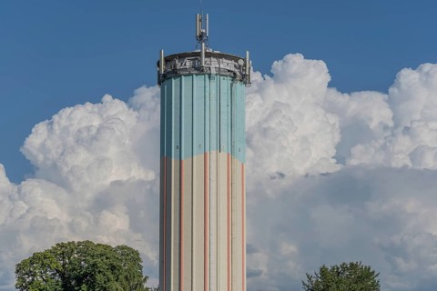 A tall water tower, painted with blue and white stripes, sits enthroned in a green landscape.