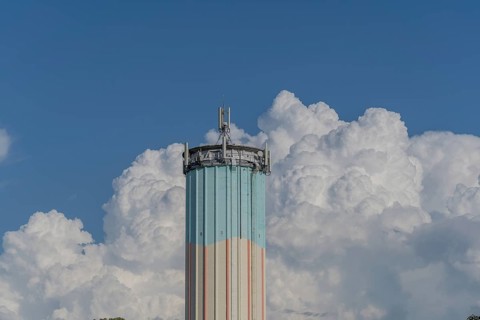 A tall water tower, painted in bright colours, rises against a backdrop of flowing white clouds.