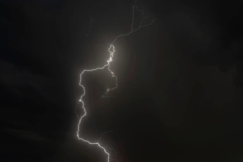 Dark clouds gather as lightning strikes light up the night. The intense storm brings thunder and