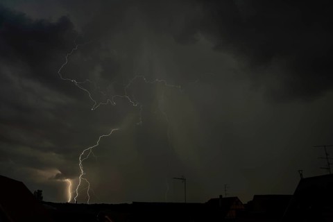 Dark clouds gather as lightning strikes light up the night above the rooftops. The intense storm