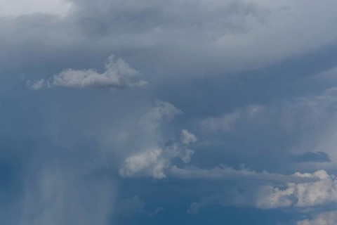 Dark storm clouds gather in the sky over a vast rural landscape, signalling an impending summer