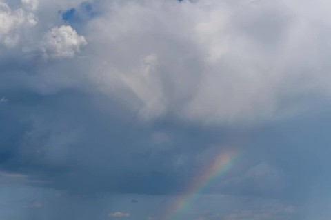 Bright sunlight breaks through large clouds after a rain shower and reveals a magnificent rainbow