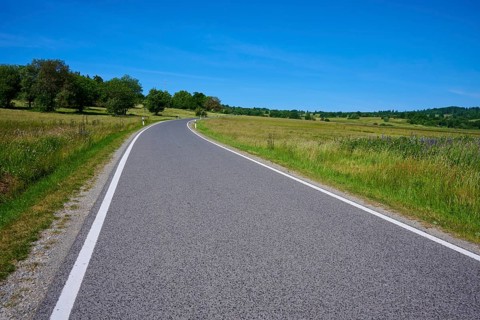Winding road through a green summer landscape with a blue sky backdrop, Franzosenweg, Lange Rhön,