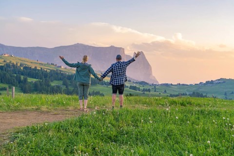 A couple raises their arms in joy at the sight of the mountain landscape and the evening sky, Alpe