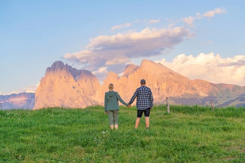 A couple stands hand in hand in a meadow in front of an impressive mountain landscape, Alpe di