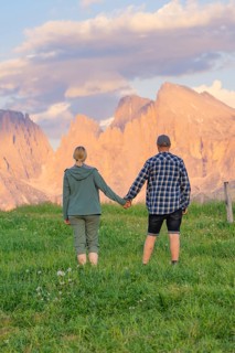 A couple holding hands in a meadow against an impressive mountain backdrop, Alpe di Siusi,