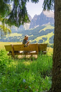 Person on a bench smiling with a peace sign in front of the mountains, Alpe di Siusi, Dolomites,