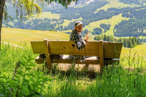 Smiling person on a bench with a peace sign in front of mountains, Alpe di Siusi, Dolomites, South