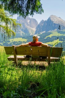 Person on a bench with a view of majestic mountains and vast landscape, Alpe di Siusi, Dolomites,