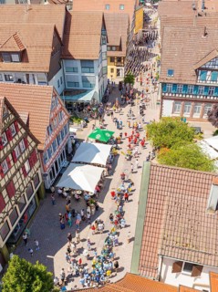 Aerial view of a busy street with half-timbered houses and cafés with parasols, many passers-by,