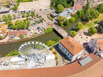 View from above of a summer festival with Ferris wheel, bridge and many people along a river in the