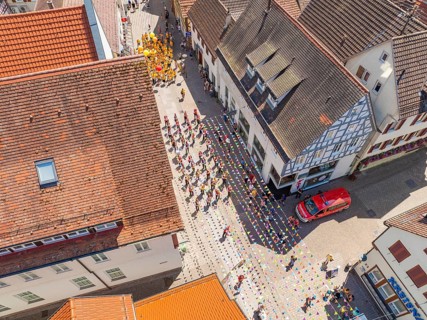Street photographed from above during a parade. People in colourful costumes, old roofs and