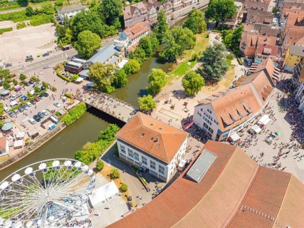 Aerial view of a summer festival with Ferris wheel, river, bridge and park, surrounded by municipal