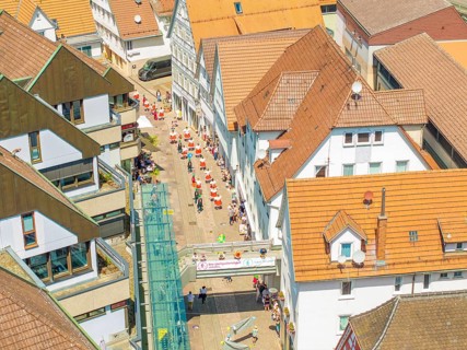Aerial view of people moving through narrow streets of a half-timbered town under a bright sun, 950