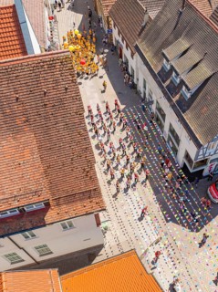 Aerial view of a colourful parade moving through the streets of a half-timbered town in the