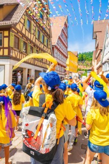 Children in yellow clothing and blue caps waving scarves in a colourful old town, 950 years of