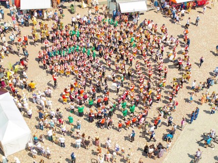 Aerial view of a festive parade on a town square with traditional costumes and a band, 950 years of