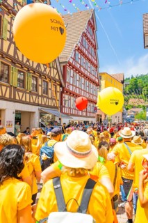 Crowd of people with orange and yellow balloons at a town festival in a half-timbered house