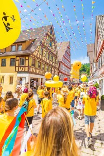 People in yellow clothes walk under colourful pennants in a narrow street in front of traditional