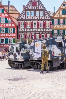 Military vehicles on a square in front of half-timbered houses, soldiers in camouflage, flowers in