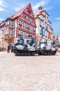 Military vehicles in front of a historic half-timbered building in a sunny old town, 950 years of