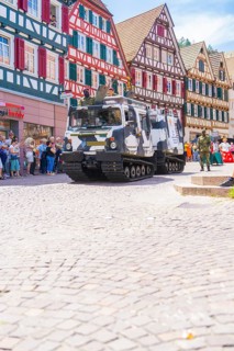 Military vehicles in a parade through a cobbled street with half-timbered houses, 950 years of