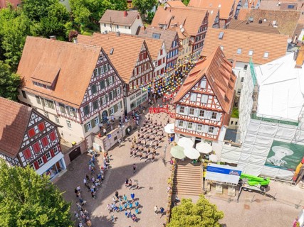 Aerial view of a town square surrounded by half-timbered houses with many people at a celebration,