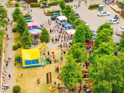 Park full of people and children's attractions with colourful tents under green trees, 950 years of