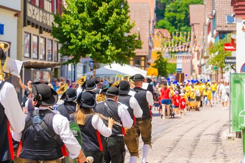People in traditional costumes musically follow a parade on a sunny village street, 950 years Calw,