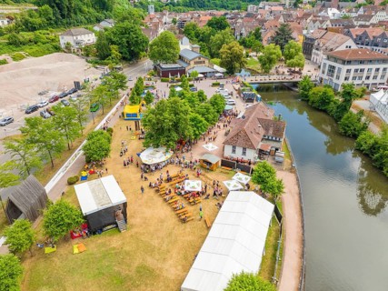 Aerial view of a town festival with people and tents on the riverbank next to historical