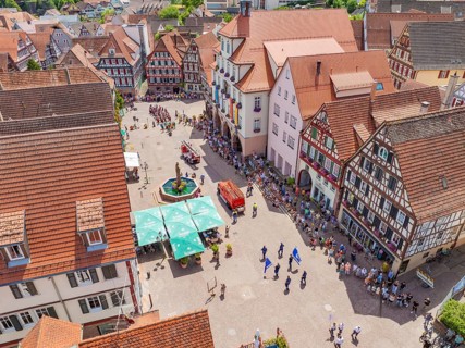 People and flags parade past on a lively market square between half-timbered houses, 950 years of
