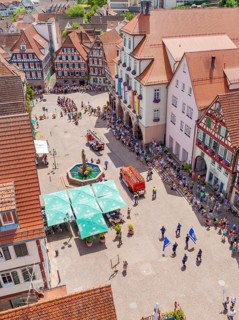 Viewed from above, a parade passes half-timbered houses around a central fountain, 950 years of