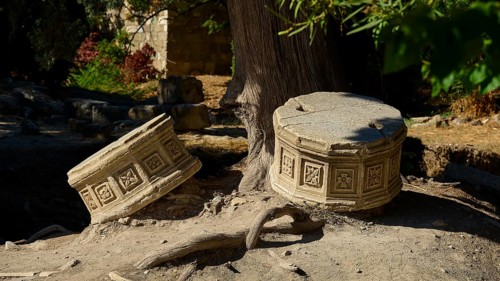 Two engraved stone cylinders resting in the shade of a tree in an ancient ruins site, Ancient